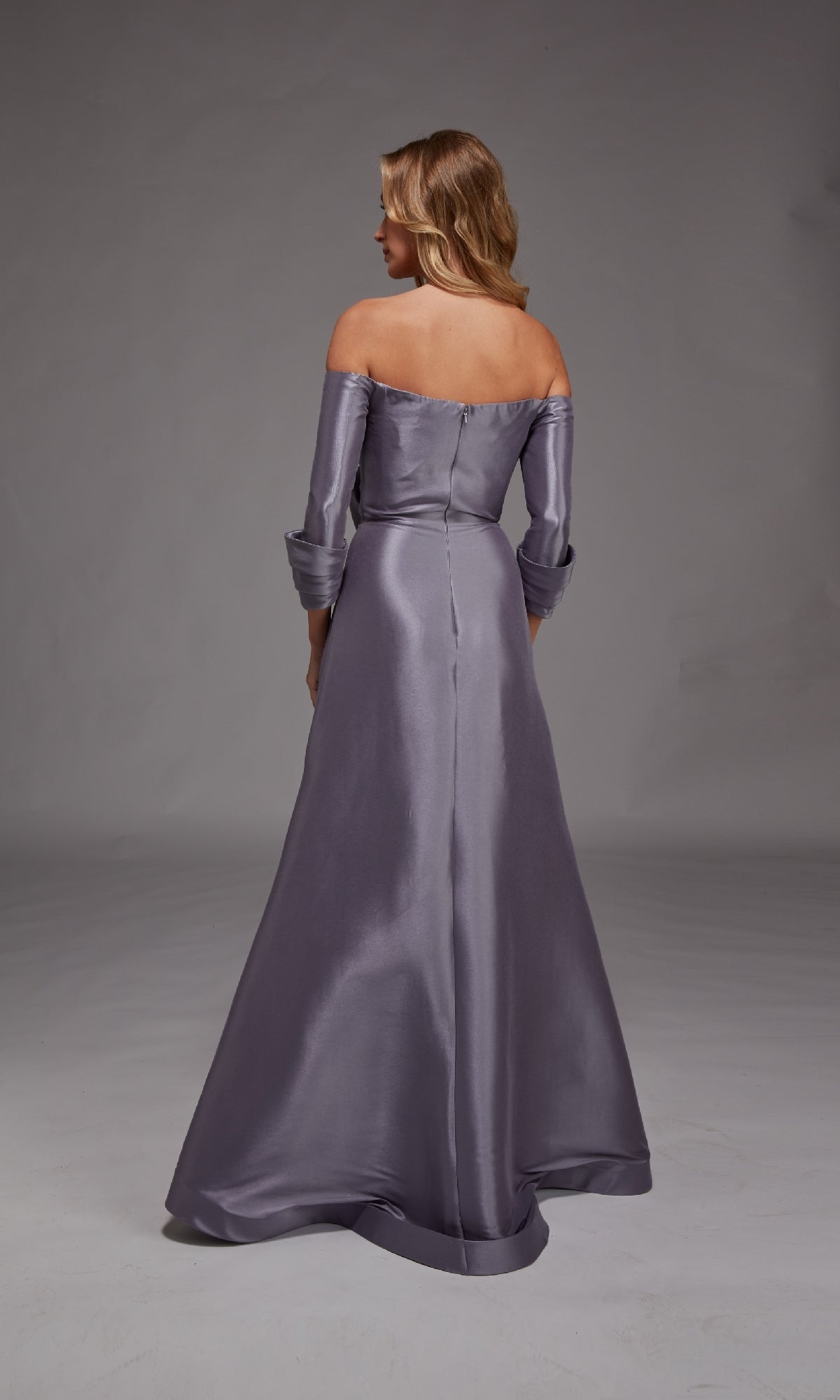 A woman in the Alyce 27859 long formal dress—an off-the-shoulder, floor-length silver-gray gown—stands with her back to the camera against a plain gray background, making an elegant mother-of-the-bride choice.